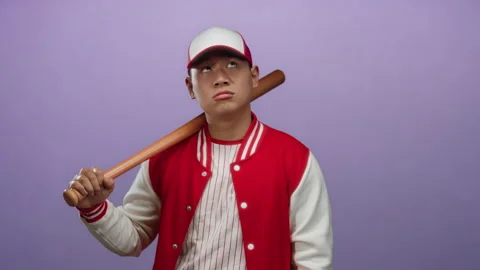 Young man in baseball uniform with bat expresses emotion against a purple b.. Stock Footage 312814455
