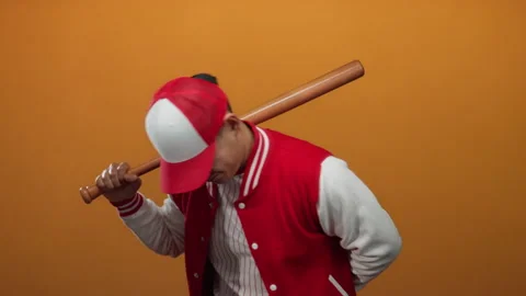 Young man in a baseball uniform poses confidently with a bat against an ora.. Stock Footage 315492987