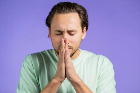 Young man in basic t-shirt praying over violet background. Guy begging someone Foto stock