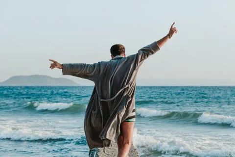 Young man in a bathrobe on the beach in sunset Stock Photos