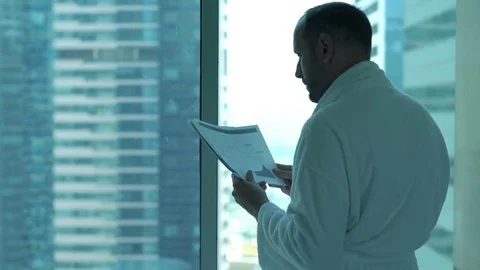Young man in bathrobe reading documents standing by window at home Vídeo Stock 70706331