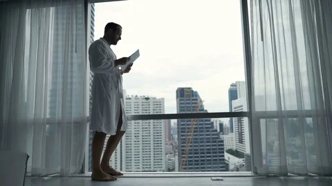 Young man in bathrobe reading documents standing by window at home Vídeo Stock 74901460