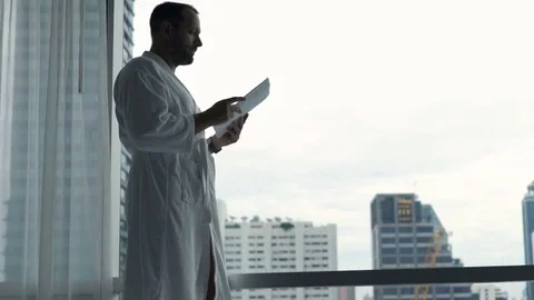 Young man in bathrobe reading documents standing by window at home Vídeo Stock 80533478