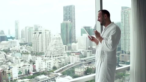 Young man in bathrobe using tablet computer standing by window at home, 240fps Stock Footage 94859229
