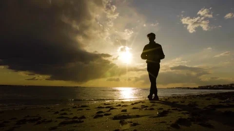 Young man on the beach at sunset. Beautiful clouds and breathtaking sunset. Slow Stock Footage 80438967