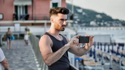 Young man on beach using cell phone to film the sea Stock Photos