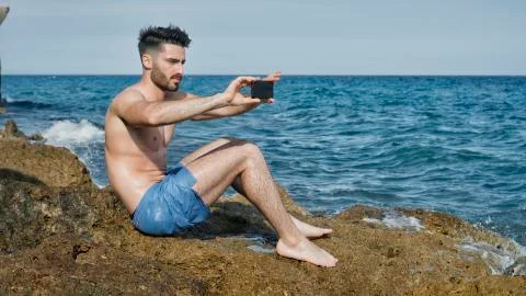 Young man on beach using cell phone to film the sea Stock Photos