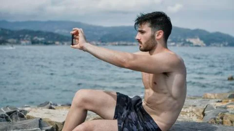 Young man on beach using cell phone to film the sea Stock Photos
