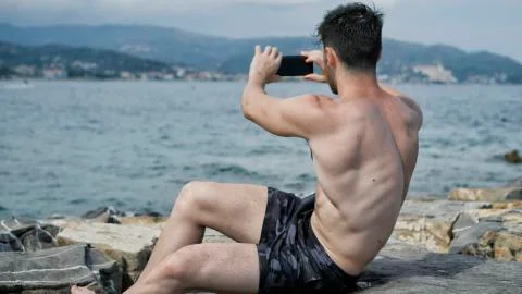 Young man on beach using cell phone to film the sea Stock Photos