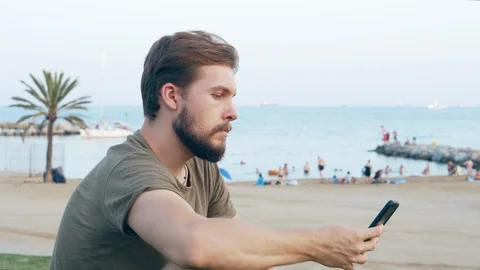 Young man on beach using smartphone Stock Footage 118936822