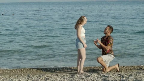 The young man on the beach wears a single stone ring to his girlfriend. Stock Footage 144329929