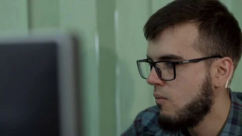 A young man with a beard and glasses works behind a computer Stock Footage 71665426