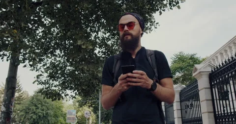 A young man with a beard and glasses looks into the phone he is holding in hand. Stock Footage 144270425