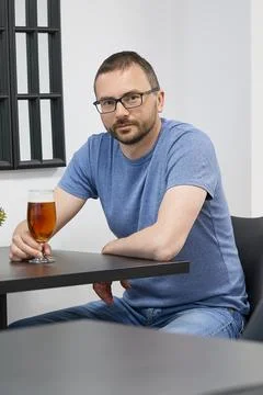 A young man with a beard and glasses drinking beer in a cafe Stock Photos