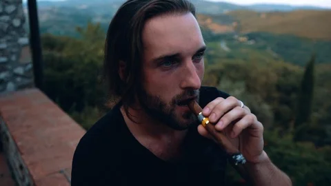 Young man with a beard and long hair smoking a cigar. Portrait, slow motion. Vídeos de archivo 108378925