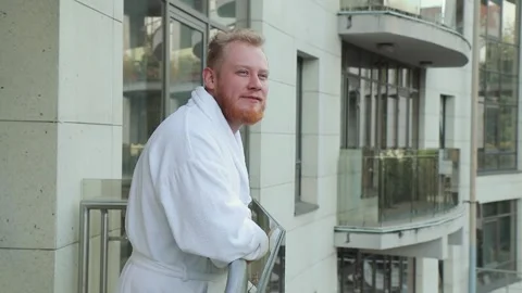 Young man with beard and in a robe rest on a hotel balcony on vacation 動画素材 147023275