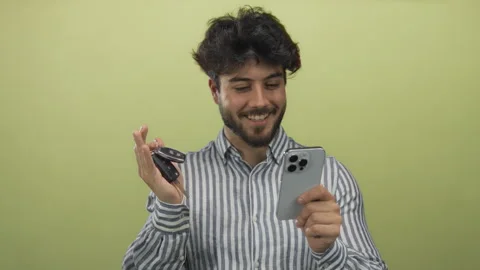 Young man with beard and striped shirt smiles while holding smartphone and .. Video stock 306843822