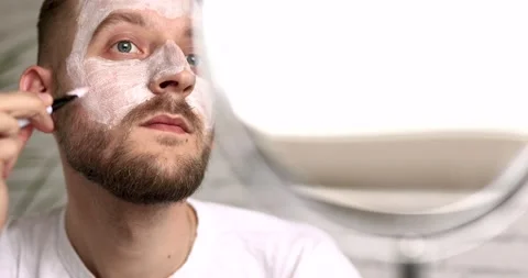 Young man with beard applying moisturising mask on face using brush after shower Stock Footage 142536778