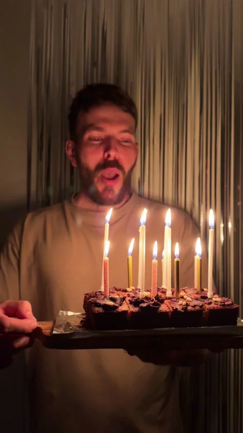 A young man with a beard is blowing out the candles on a birthday cake Stock Footage 342268748