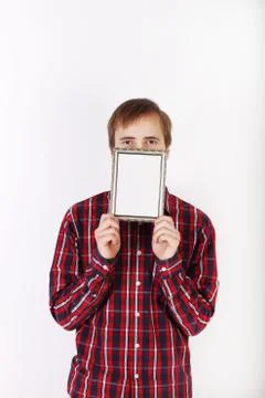 Young man with beard in checkered red shirt hides his mouth behind frame Stock Photos