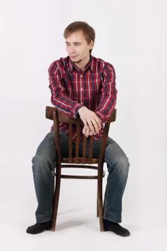 Young man with beard in checkered red shirt sits astride chair and looks away Stock Photos