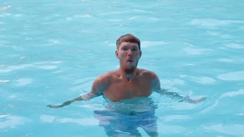 A young man with a beard dives and comes up with a splash in the pool with clear Stock Footage 70774839