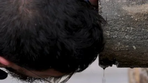 Young man with beard drinking from the potable water spout of a stone Vidéo 196178869