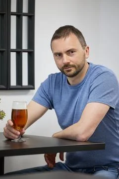 A young man with a beard drinks beer from a glass in a cafe Stock Photos