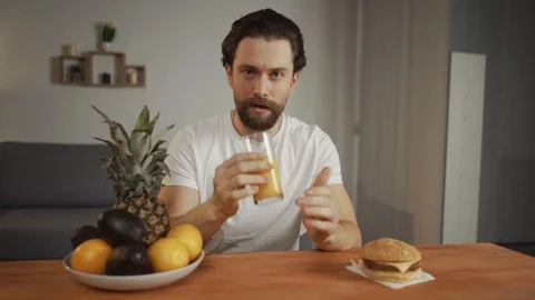 Young man with a beard drinks orange juice, smiles, chooses a healthy lifestyle Stock Footage 127384123