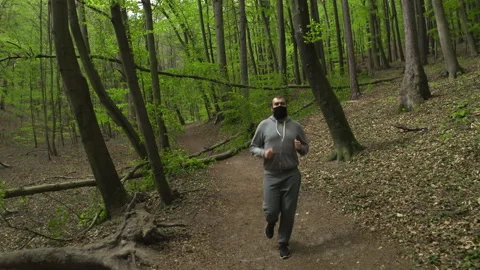 Young Man with Beard in Face Mask in Sportswear Running in a Lush Forest Stock Footage 130762341