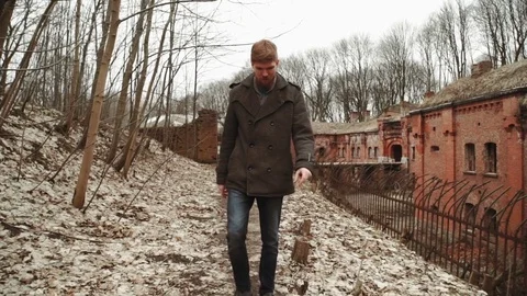 A young man With a beard, in a gray coat walks through the park in the spring or Stock Footage 74128992