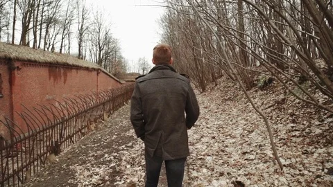 A young man With a beard, in a gray coat walks through the park in the spring or Stock Footage 74133780