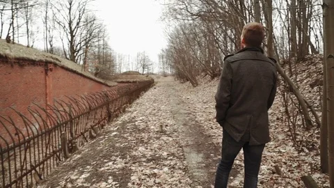 A young man With a beard, in a gray coat walks through the park in the spring or Stock Footage 74135467