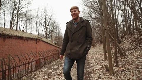 A young man With a beard, in a gray coat walks through the park in the spring or Stock Footage 74136578