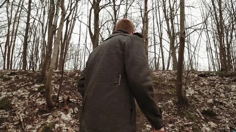 A young man With a beard, in a gray coat walks through the park in the spring or Stock Footage 74136941