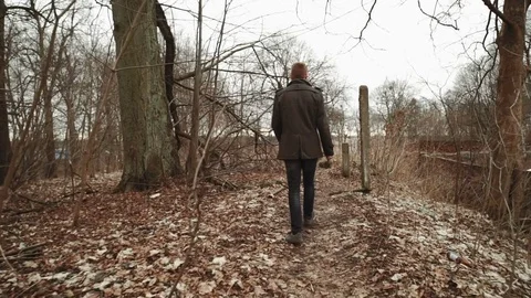 A young man With a beard, in a gray coat walks through the park in the spring or Stock Footage 74137511