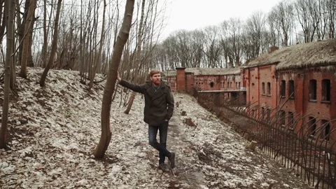 A young man With a beard, in a gray coat walks through the park in the spring or Stock Footage 74139165