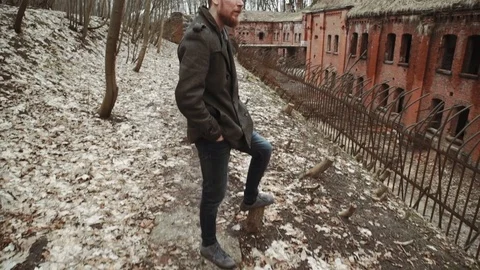 A young man With a beard, in a gray coat walks through the park in the spring or Stock Footage 74139306