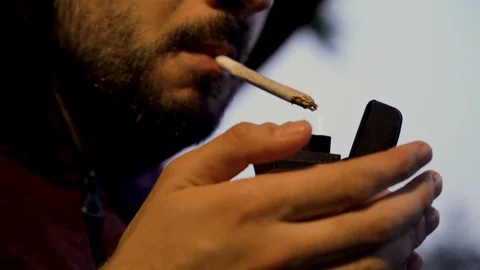 Young man with beard lighting a weed joint outdoors, close shot Stock Footage 111650970