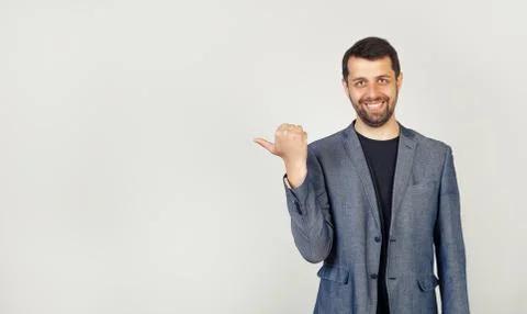 The young man with a beard, looking and pointing to the side with a thumb Foto stock