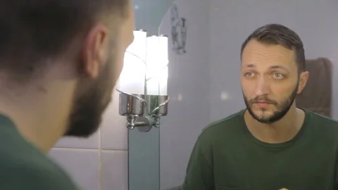 Young man with beard looking at mirror, wiping his face with a towel Stock Footage 104022107