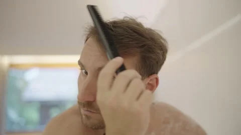 Young man with a beard looking in the mirror while styling his hair with a comb Stock-Footage 335204073