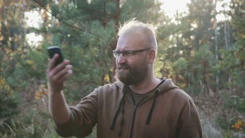 A young man with a beard looking for a mobile phone signal in the woods Stock Footage 98675073