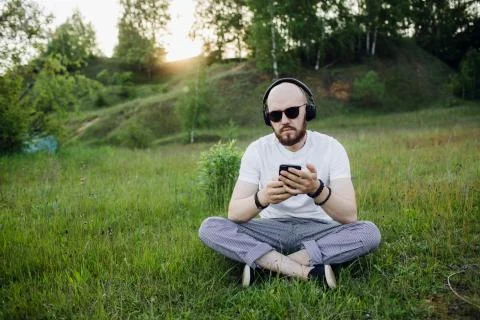Young man with beard lying on grass and listening music Foto stock