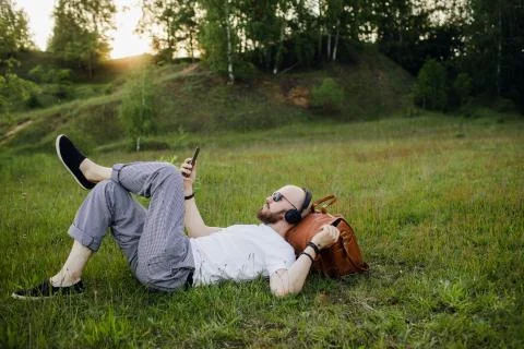 Young man with beard lying on grass and listening music Фото