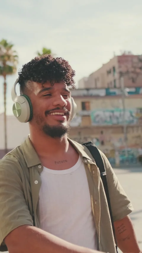 Young man with beard in an olive-colored shirt listens to music on headphones, Stock Footage 226462142