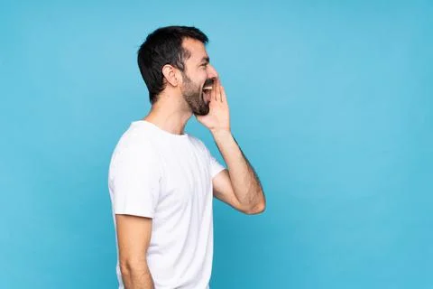 Young man with beard  over isolated blue background shouting with mouth wide  Photos