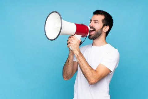 Young man with beard  over isolated blue background shouting through a megaph Stock Photos