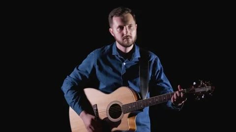 Young man with a beard playing acoustic guitar. Black background. Isolated Stock Footage 135234841