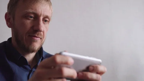 Young man with a beard plays the game on his phone Stock Footage 128298259